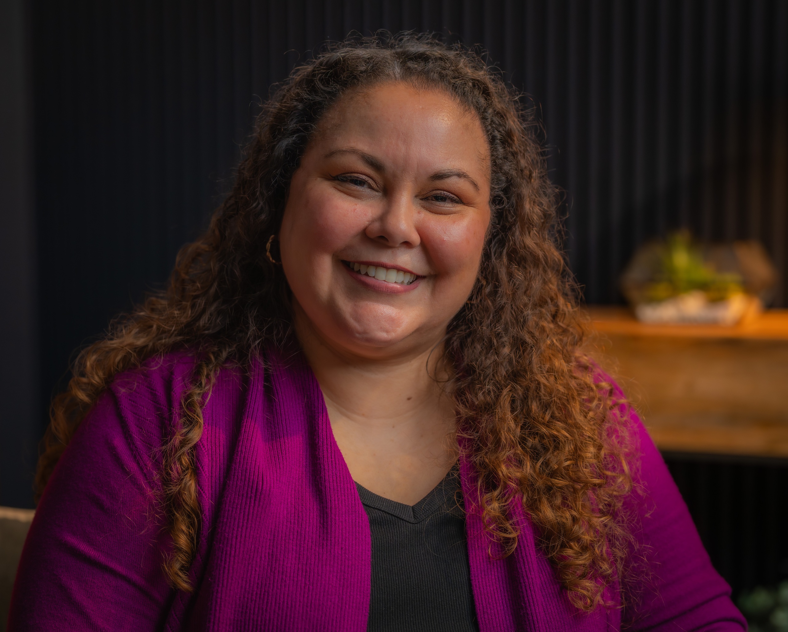 Headshot of Jackie Valenzuela wearing a black top with a magenta cardigan and smiling.